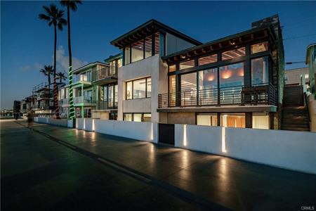 Modern two-story waterfront homes with large glass windows and palm trees at dusk along a lighted street.